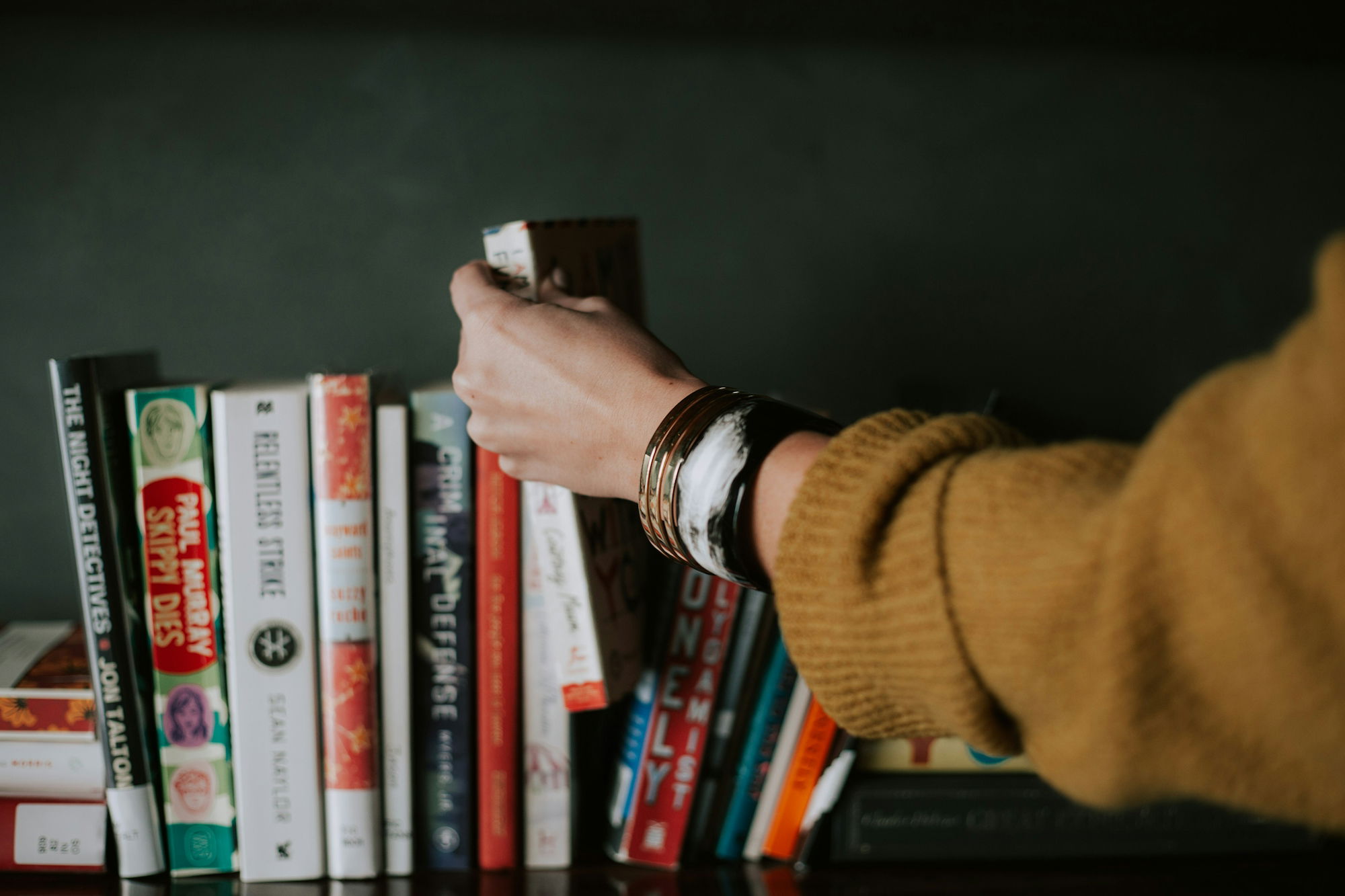 person-picking-white-and-red-book-on-bookshelf.jpg person picking white and red book on bookshelf